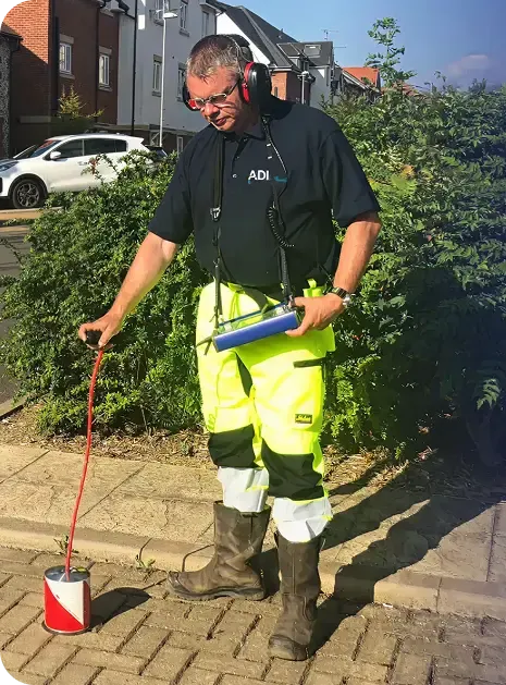 ADI engineer wearing headphones and using acoustic leak-detection equipment on a paved path